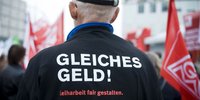 Kapitalismuskongress II Von hinten fotografierter Mann, auf dessen Jacke "Gleiches Geld" steht.
