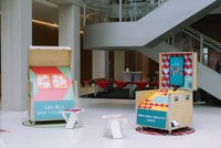 Das Bild zeigt Teile der Ausstellung "Vielfalt ist Freiheit" mit zwei Informationsständen in einem modernen Gebäude. Der linke Stand trägt die Aufschrift "Lexikon der Vielfalt" und ist mit bunten geometrischen Mustern gestaltet. Er enthält mehrere Informationskarten, die vermutlich Themen zur Vielfalt und Inklusion abdecken. Der rechte Stand ist als "Gewerkschaftshaus" bezeichnet und zeigt einen Bildschirm mit dem Text "Bitte klingeln. Vielfalt erleben". Beide Stände sind Teil einer Präsentation, die auf die Förderung von Vielfalt und gewerkschaftlichen Anliegen abzielt.