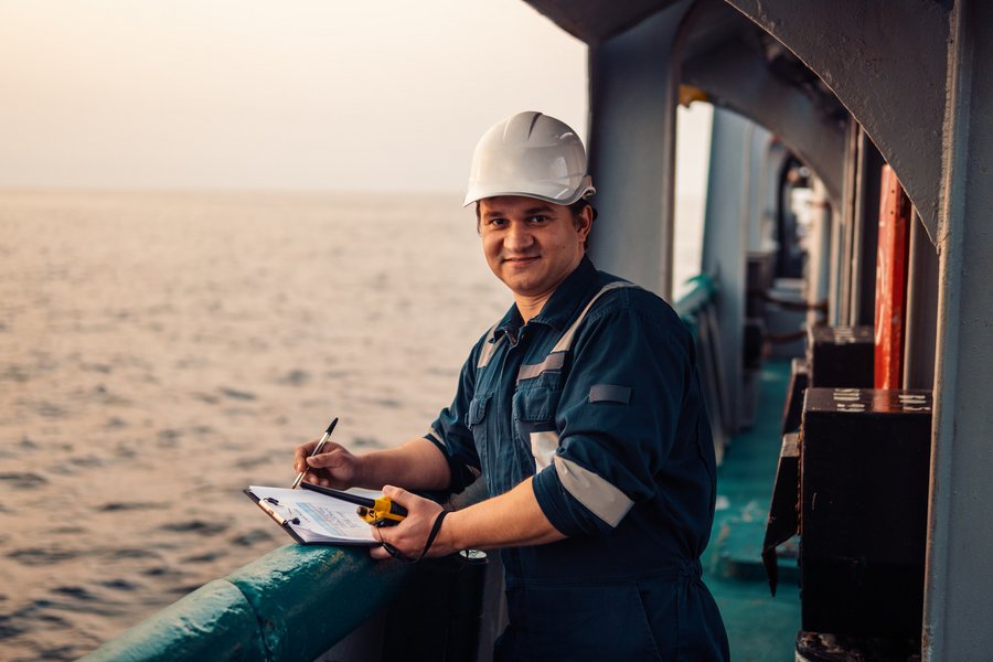 Arbeiter_Industrie Deckoffizier an Deck eines Offshore-Schiffes oder -Schiffes, der persönliche Schutzausrüstung trägt. Er füllt Checkliste. Papierkram auf See