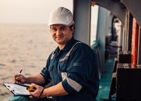 Arbeiter_Industrie Deckoffizier an Deck eines Offshore-Schiffes oder -Schiffes, der persönliche Schutzausrüstung trägt. Er füllt Checkliste. Papierkram auf See