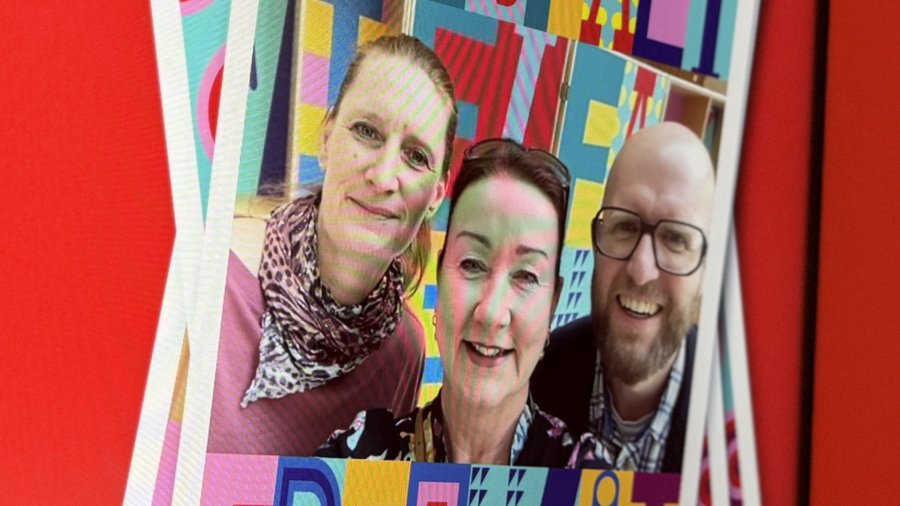 Das Bild zeigt einen Bildschirm, auf dem mehrere übereinanderliegende Selfies abgebildet sind. Die oberste Karte trägt die Wörter "Vielfalt Freiheit" in bunten, stilisierten Buchstaben. Der Hintergrund des Bildschirms ist rot, und links neben dem Bildschirm befindet sich Text, der Informationen über die Nutzung eines QR-Codes für den Zugang zu einer Online-Galerie und die Möglichkeit zur Teilnahme auf Social Media bietet. Die Gestaltung ist lebendig und auffällig, um das Thema Vielfalt und Gemeinschaft zu betonen. Der Text "Gemeinsam stark" ist ebenfalls sichtbar und unterstreicht die Botschaft der Einheit und Stärke.